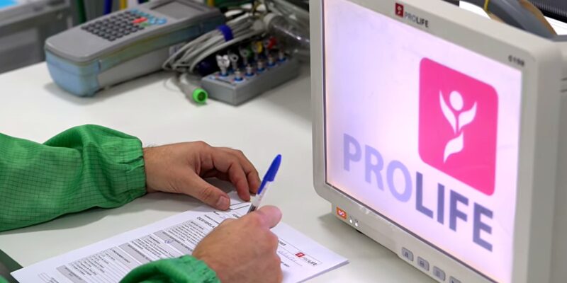 Colaborador da ProLife preenchendo registro de inspeção de qualidade ao lado de monitor multiparamétrico
